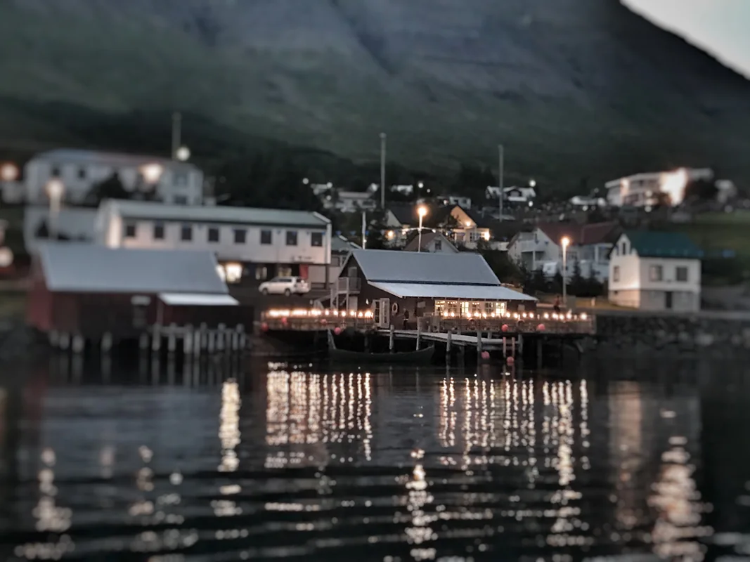 Beituskúrinn og upplýst veröndin við sjóinn speglast í vatninu.